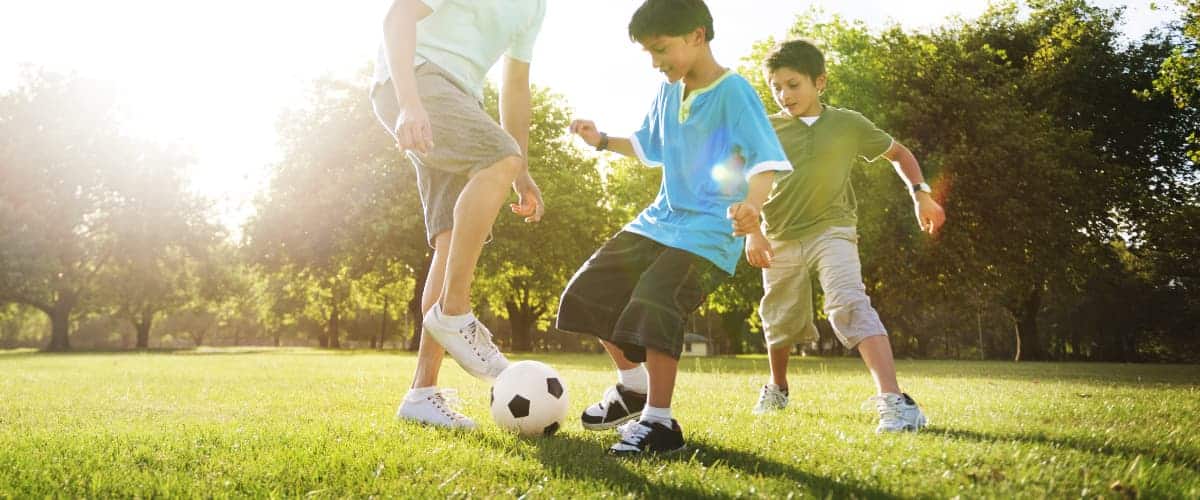 Two brothers kick a soccer ball around with their dad