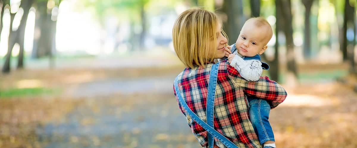 A mother in overalls carries her baby in the park