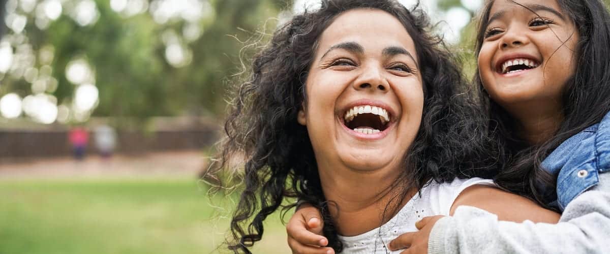 A laughing Latina mother carries her little girl on her shoulders